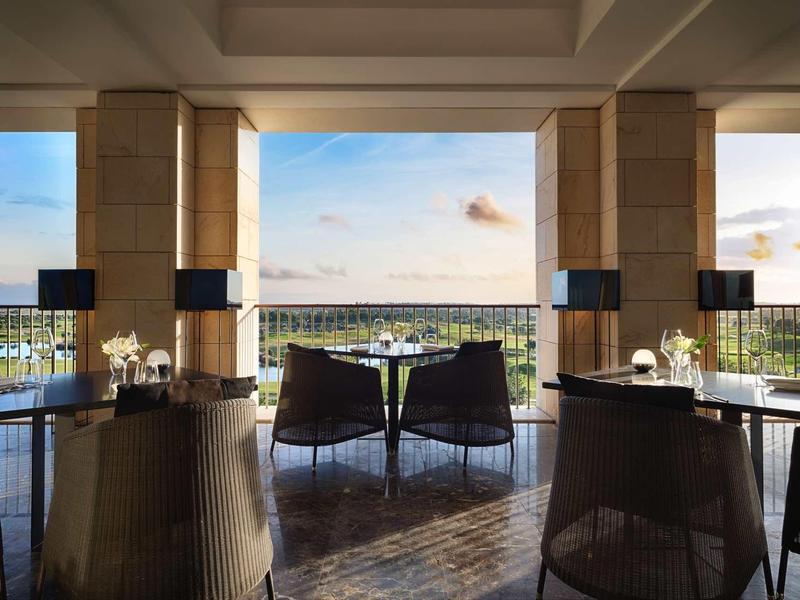 Moderner Essbereich mit dunklen Stühlen, Tischen und offenem Blick auf eine Aussicht unter blauem Himmel.