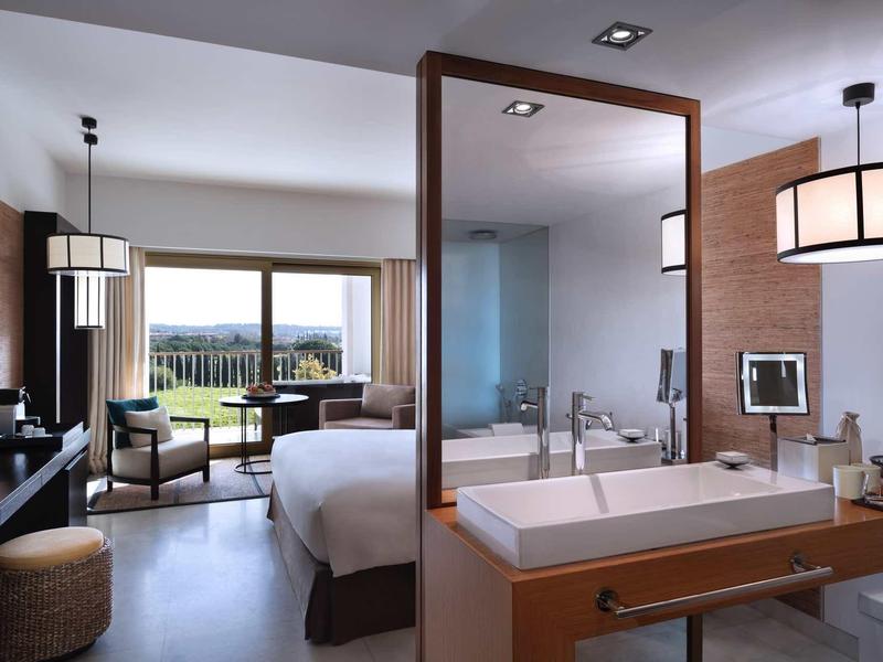 Moderner Hotelraum mit Doppelbett, Sitzecke, Holztrennwand und großem Fenster mit Blick ins Freie.