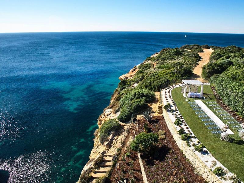 Küstenklippe mit grasbedecktem Pfad und Blick auf das tiefe blaue Meer unter klarem Himmel.