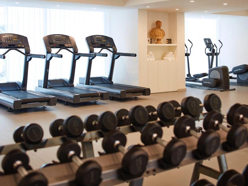 Modernes Fitnessstudio mit Laufbändern, Ellipsentrainern und Reihen von Kurzhanteln in hellem Raum.