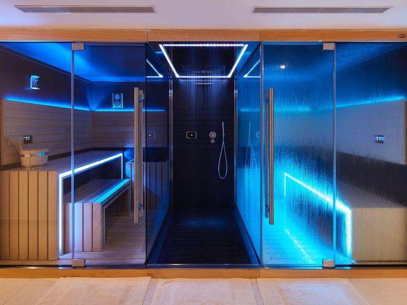Moderne Sauna mit Glasfront, LED-Beleuchtung in Blau und Holzverkleidung, stilvoll und einladend.