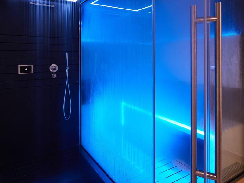 Moderner, dunkler Duschraum mit blauer LED-Beleuchtung und gläserner Tür mit Metallgriff.