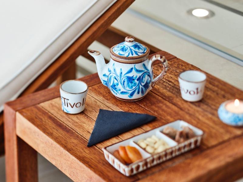 Braune Holzablage mit blau-weißer Teekanne, zwei Tassen, schwarzem Serviette und Snackschale.