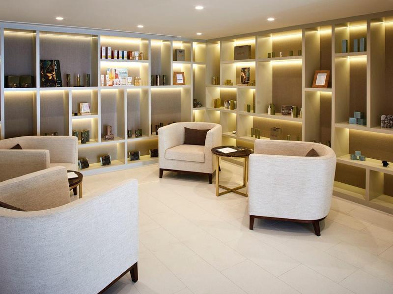 Helles, modernes Wartezimmer mit beigen Sesseln, goldenen Tischen und dekorativ beleuchteten Regalen.