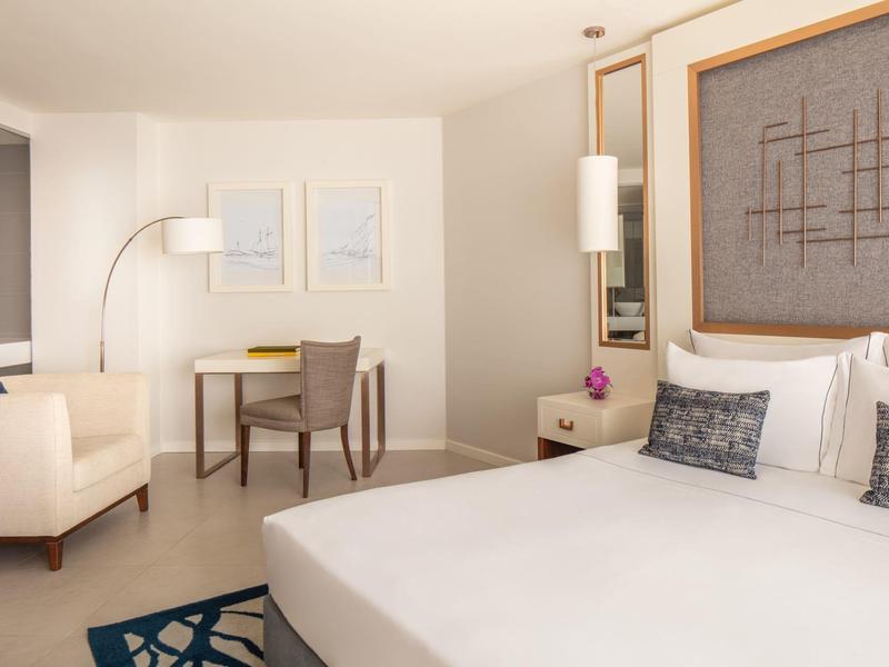 Helles Schlafzimmer mit großem weißen Bett, Lederstuhl, Schreibtisch, Sofa und modernen Wandbildern.