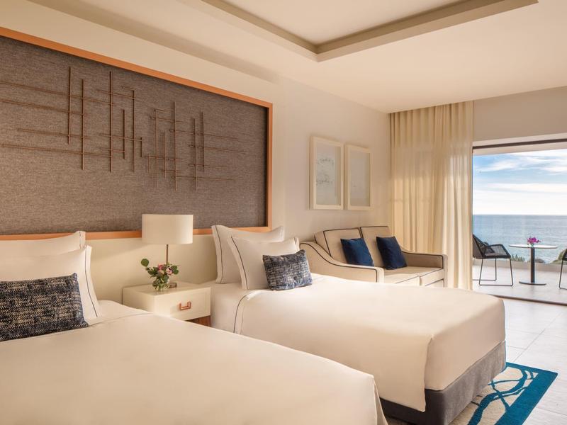 Helles Hotelzimmer mit zwei Doppelbetten, modernem Dekor, Balkon und Meerblick.