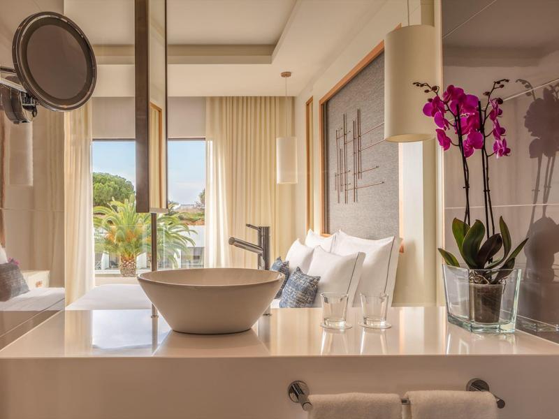 Modernes Hotelzimmer mit Waschbecken, Blumen und Balkon mit Blick ins Grüne.