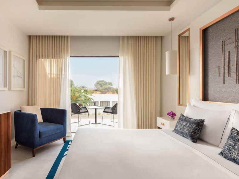 Modern eingerichtetes Schlafzimmer mit großem Bett, Balkon und blauem Sessel.