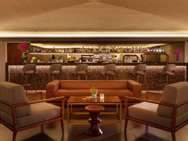 Modern eingerichtete Bar mit braunen Sesseln, Holztisch und beleuchtetem Tresen im Hintergrund.