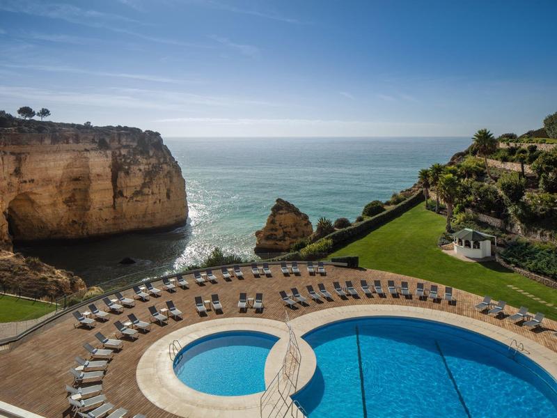 Blick auf Swimmingpools, Rasenfläche und Küste mit Felsen unter blauem Himmel an der Meeresküste.