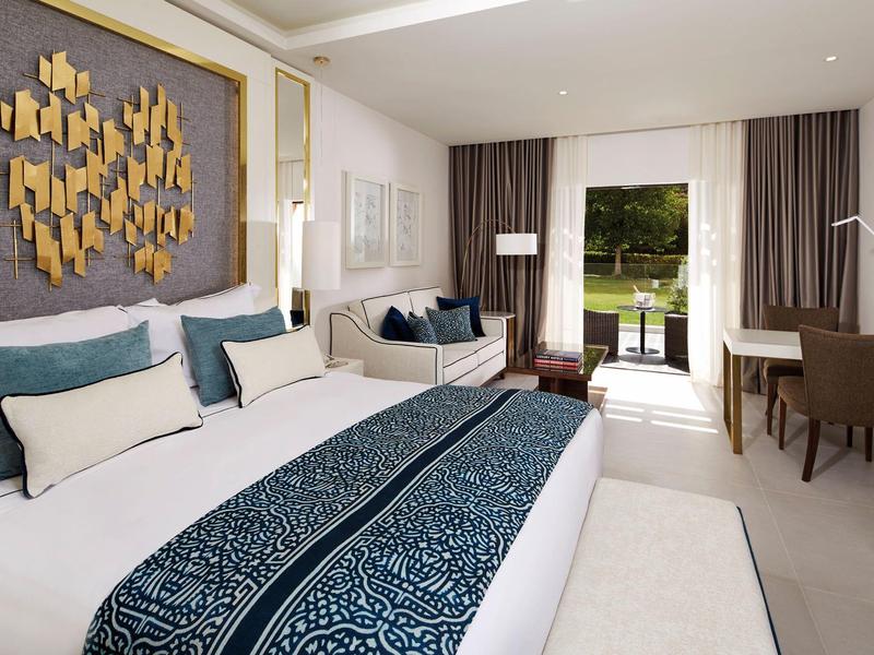 Modernes Schlafzimmer mit großem Bett, blau-weißer Bettwäsche, Sofa und Zugang zum Garten.