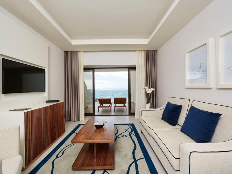 Modernes Wohnzimmer mit weißem Sofa, blauen Kissen, Holztisch, Teppich und TV an der Wand.