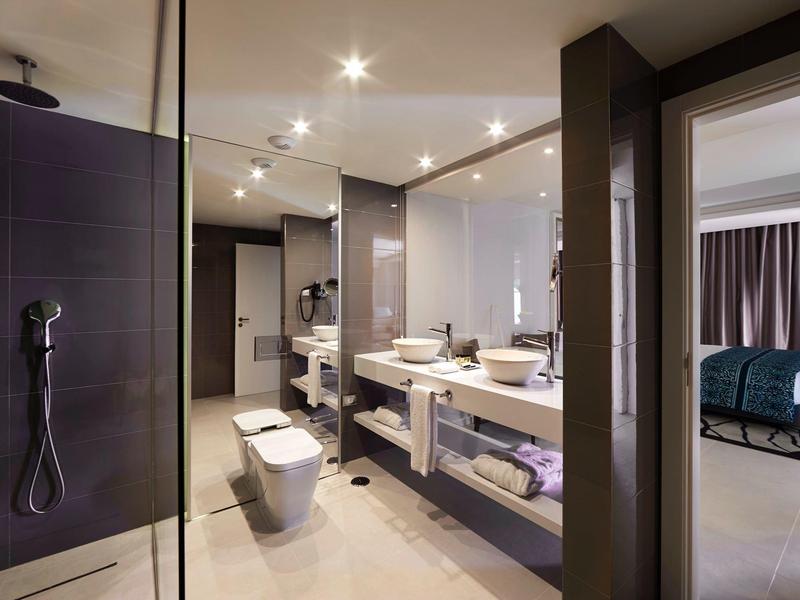 Modernes Badezimmer mit Doppellavabo, begehbarer Dusche, WC und Blick ins Schlafzimmer.