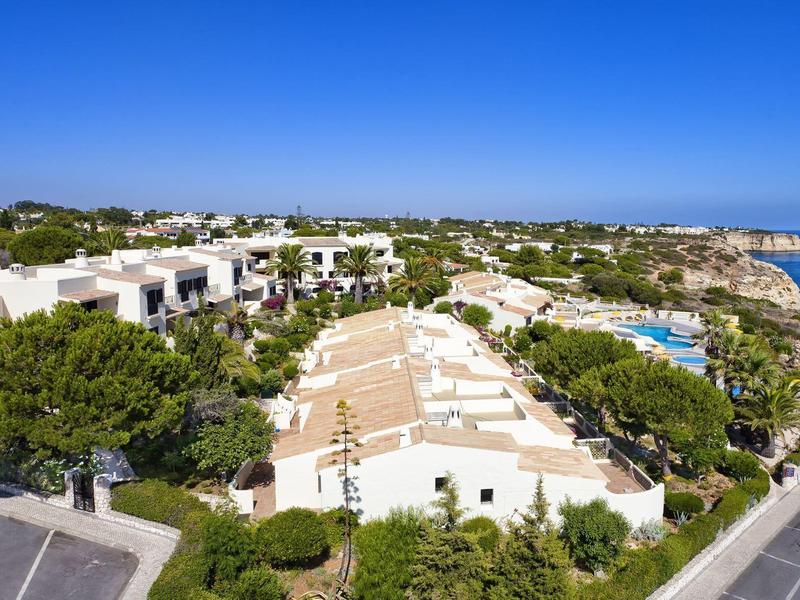 Landschaft mit weißen Gebäuden, grünem Bewuchs, blauem Himmel und Meer am Horizont.