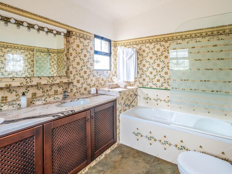 Helles Badezimmer mit gemusterten Fliesen, Doppelwaschbecken, Holzschrank und Badewanne mit Glaswand.