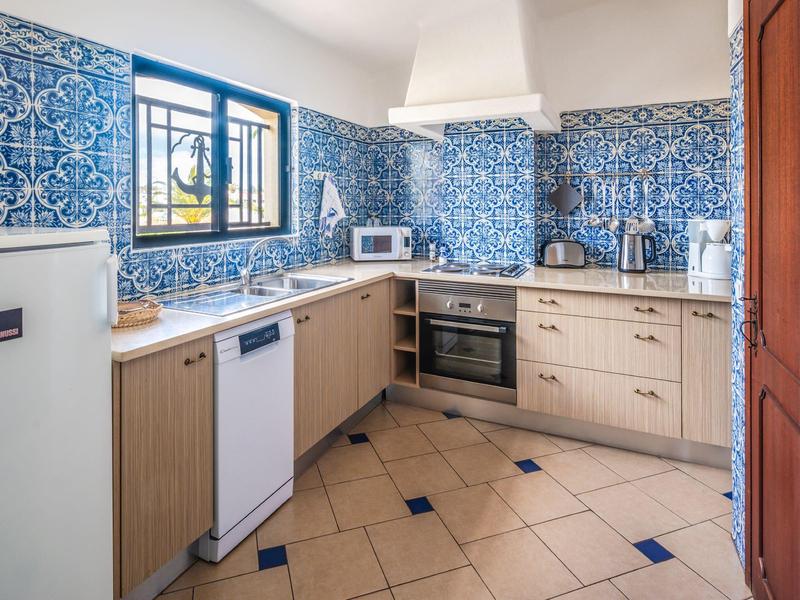 Helle Küche mit blauen Wandfliesen, Holzschränken, weißen Geräten und gefliestem Boden mit blauen Akzenten.