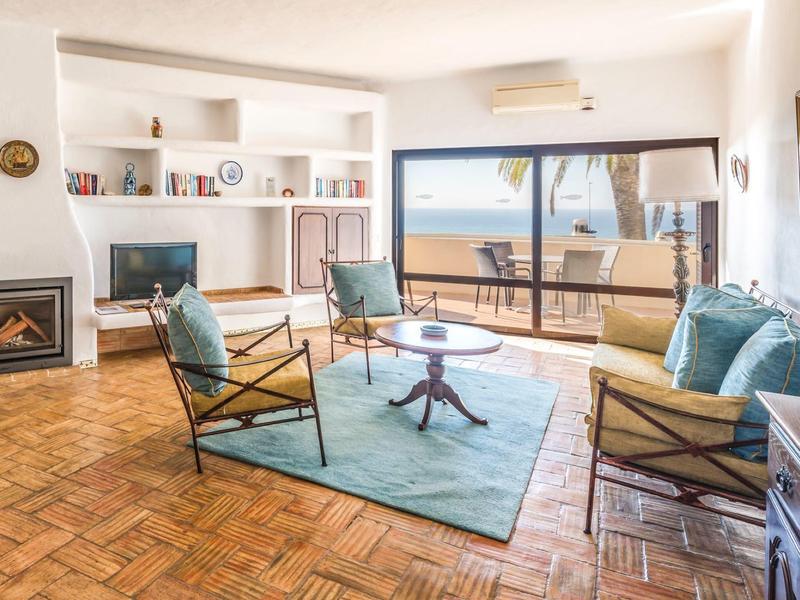 Helles Wohnzimmer mit Parkettboden, Kamin, blauen Sesseln und großem Fenster mit Meerblick.