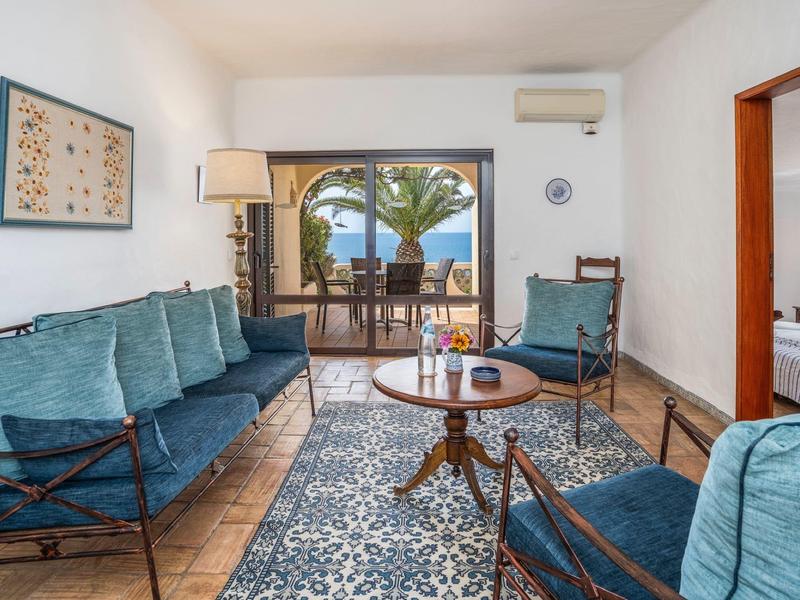 Helles Wohnzimmer mit blauen Sitzmöbeln, Holztisch, Teppich und Blick auf Terrasse mit Palmen.