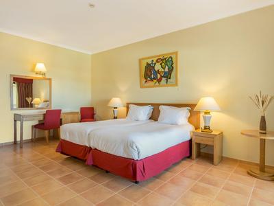 Hell eingerichtetes Schlafzimmer mit Doppelbett, roten Akzenten und zwei Nachttischen mit Lampen.