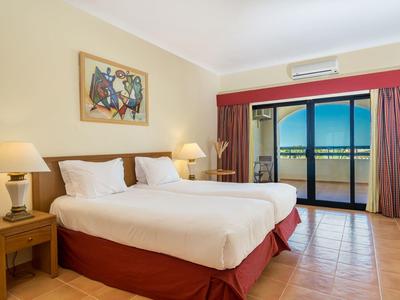 Hell eingerichtetes Schlafzimmer mit Doppelbett, Nachttischen, Lampen und Balkon mit Meerblick.