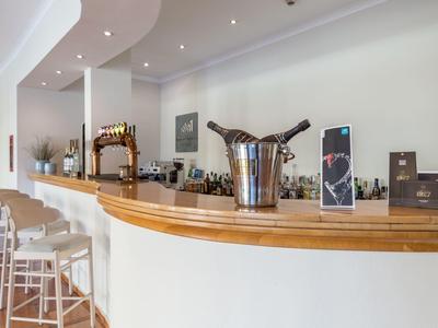 Moderner Barbereich mit hellem Holz, weißen Hockern und Eisbehälter auf Theke.