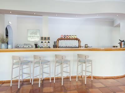 Moderne Bar mit hellen Holzstühlen, stilvollem Tresen und weißer Wand im hellen Raum.