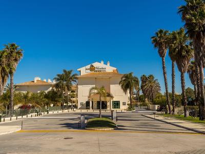 Großes gelbliches Gebäude mit Palmen und blauem Himmel im sonnigen Umfeld.