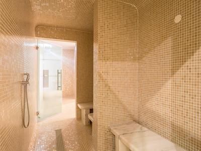 Moderner Dampfraum mit kleinen beigen Mosaikfliesen, Sitzbänken und Handbrause an der Wand.