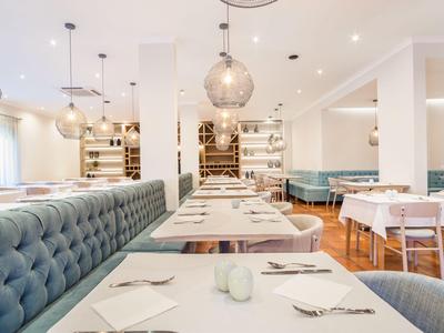 Modern eingerichtetes Restaurant mit blauen Polstersesseln und weißen Tischen in hellem Raum.