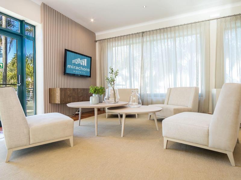 Helles Wohnzimmer mit großen Fenstern, vier cremefarbigen Sesseln und zwei runden Tischen.