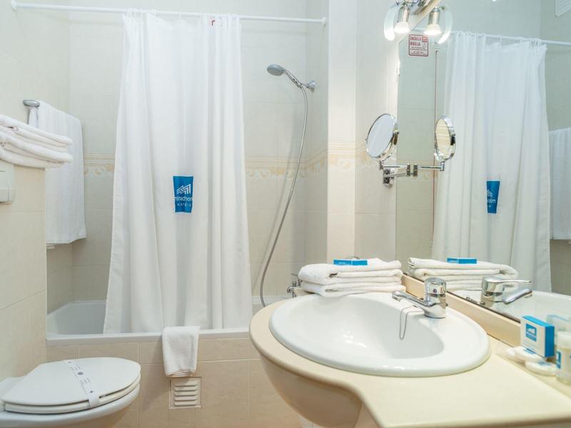 Helles Badezimmer mit weißem Vorhang, Waschbecken, Toilette und Handtüchern.