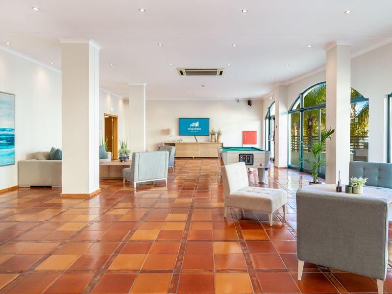 Heller, geräumiger Aufenthaltsraum mit großen Fenstern, weißen Wänden und Terrakottaboden.