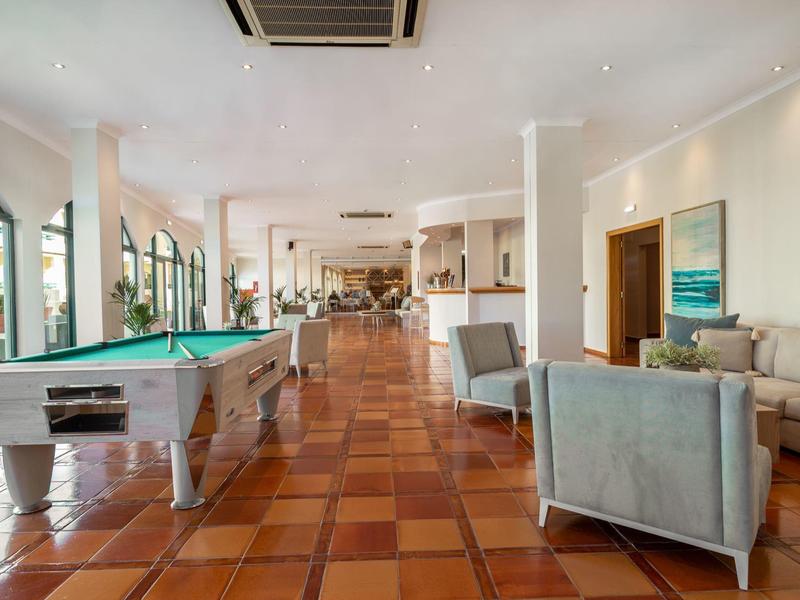 Großer Aufenthaltsraum mit Billardtisch, grauen Sesseln, Terrakottaboden und großen Fenstern.