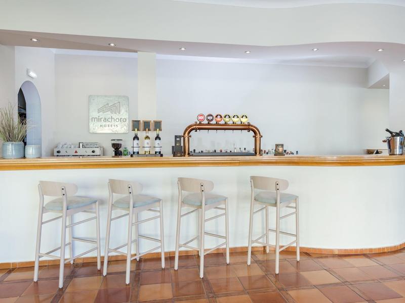 Moderne Bar mit hellen Holzstühlen, stilvollem Tresen und weißer Wand im hellen Raum.