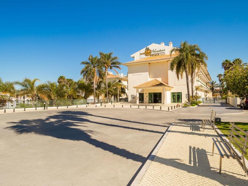 Großer Platz mit Palmen und hellem Gebäude unter klarem blauem Himmel am Tag.
