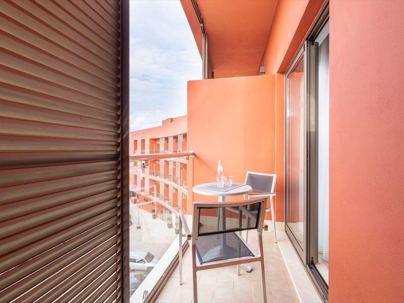 Balcón pequeño con mesa, silla y vaso en un edificio de hotel naranja.