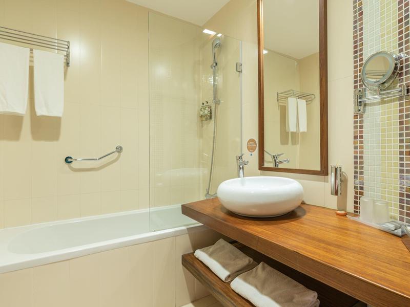 Baño moderno con bañera, lavabo redondo y mesa de madera con toallas.