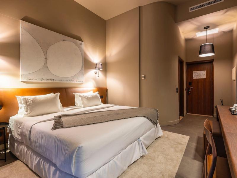 Habitación de hotel moderna con cama doble, luz cálida y decoración sencilla.