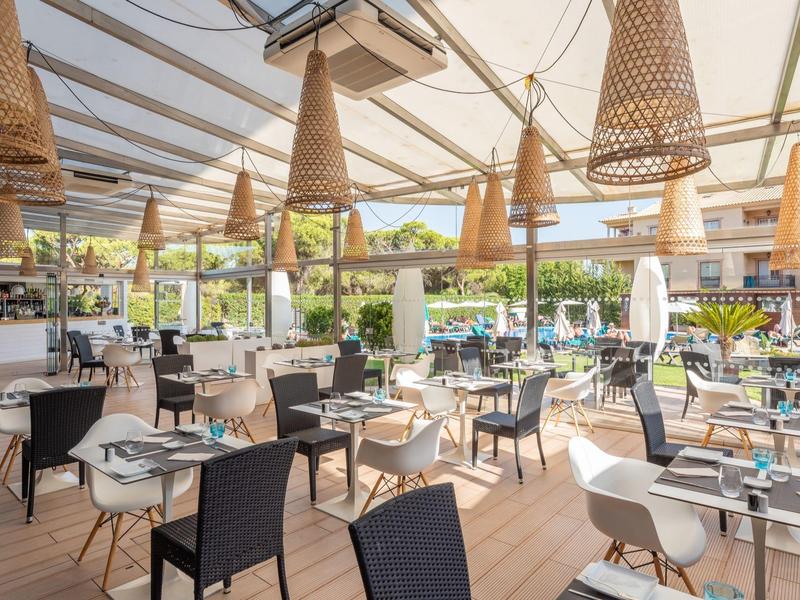 Restaurante luminoso con arreglos de mesas modernas y lámparas de mimbre bajo un techo transparente.