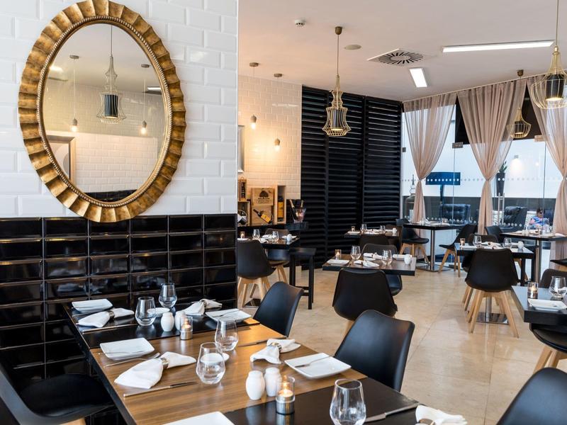 Restaurante moderno con elementos de madera y negro, mesas puestas y espejo redondo en la pared.