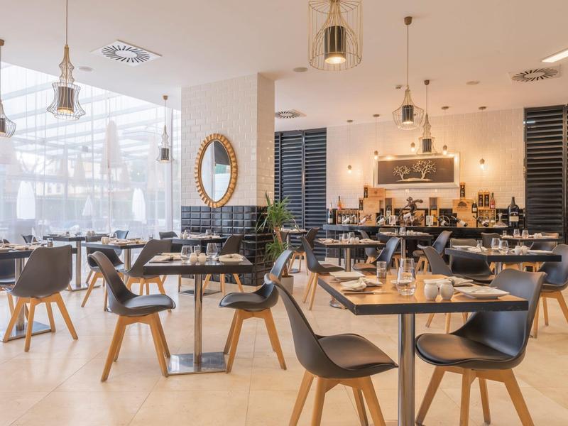 Restaurante luminoso con sillas negras modernas, mesas de madera y iluminación elegante.