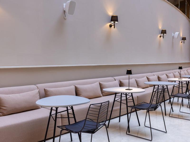 Área de asientos moderna con sofás largos, mesas pequeñas y sillas negras bajo luces de pared.