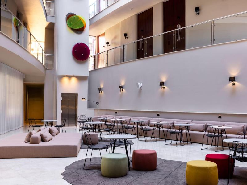 Área de lounge moderna en hotel con pufs, taburetes acolchados y iluminación acogedora.