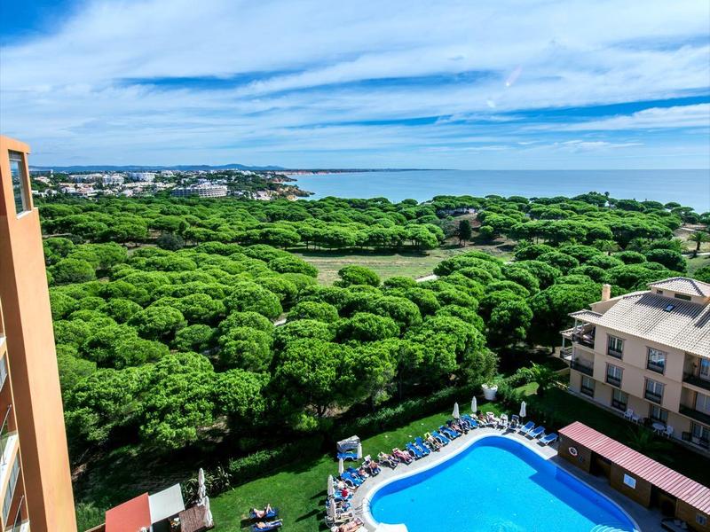 Habitación de hotel luminosa con dos camas, mesitas, lámparas de pared y balcón con vista.