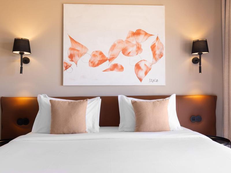Habitación de hotel moderna con cama blanca, cojines marrones y cuadro de peces sobre el cabecero.