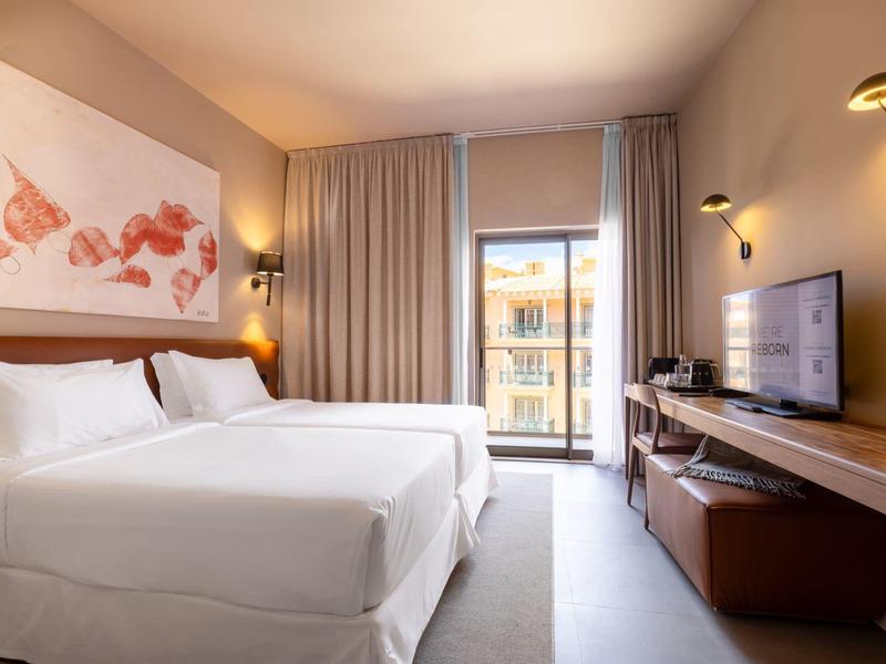 Habitación de hotel moderna con dos camas, ventana grande e interior minimalista.