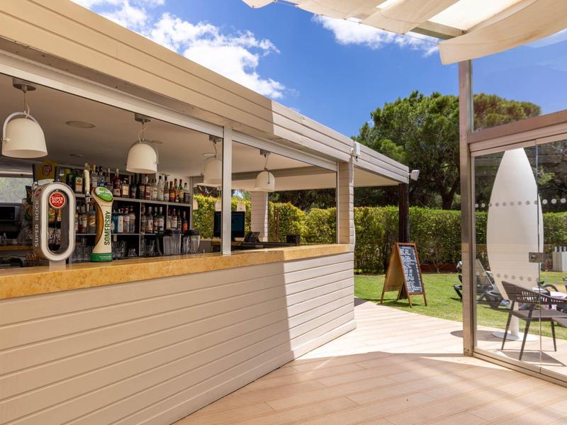 Área de bar al aire libre moderna con mostrador de madera y asientos bajo cielo azul.