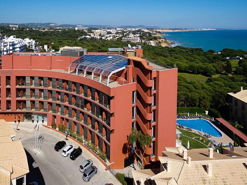 Edificio de hotel rojo en forma de arco con piscina y vista costera bajo cielo despejado.