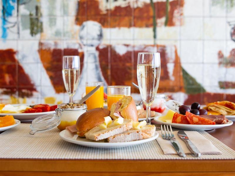 Stół śniadaniowy z rogalikiem, sokiem pomarańczowym i szampanem na tle kolorowej dekoracji ściennej.