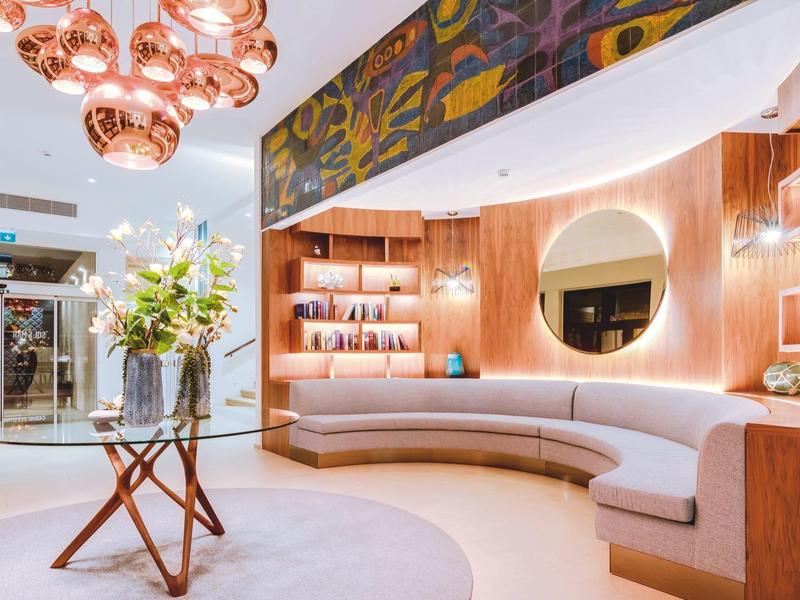 Jasna lobby hotelowa z zakrzywioną częścią siedzącą, drewnianą boazerią i nowoczesnym wystrojem.